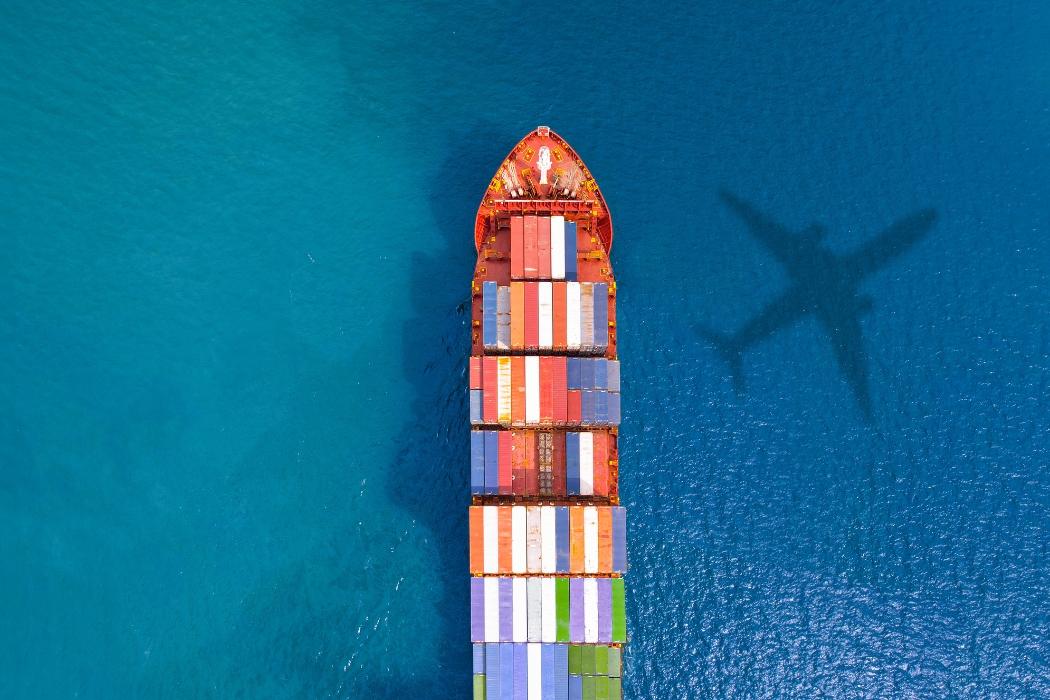 Aerial of container ship at sea with shadow of cargo plane
