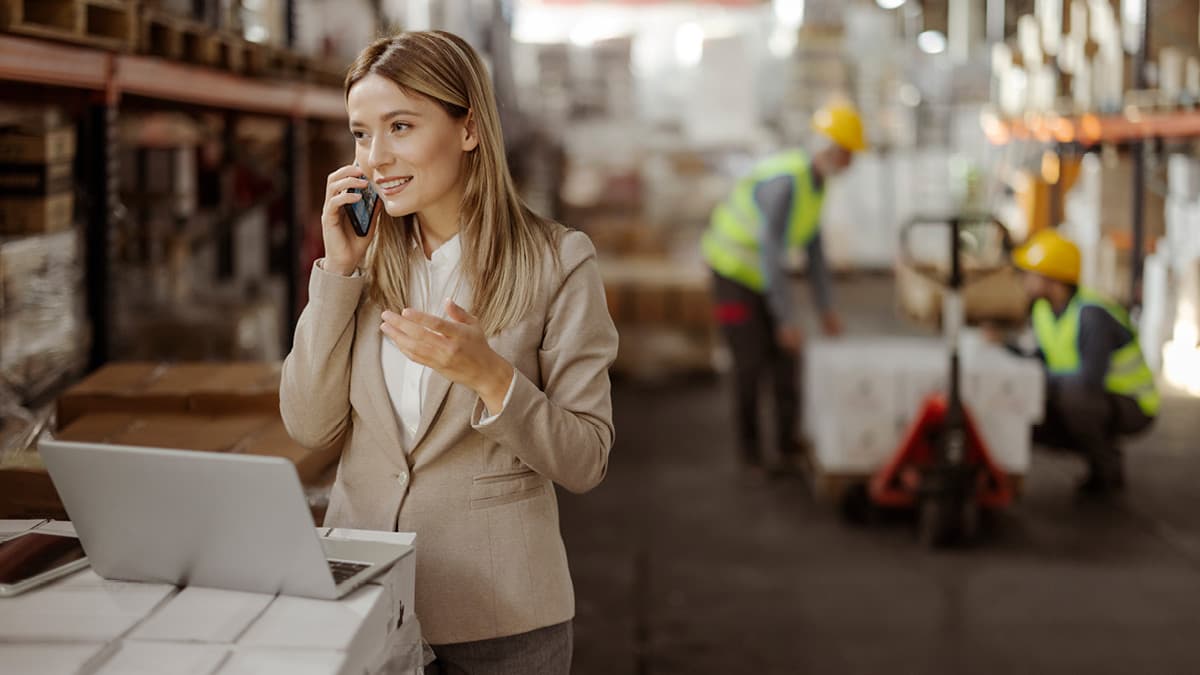 Woman on the phone with laptop in front of her. In a warehouse.