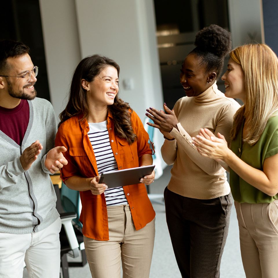 Group of coworkers gathered clapping for another coworker who's holding a tablet.