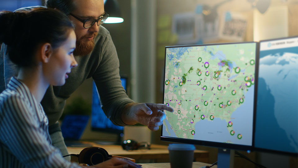 Man and woman huddled around Navisphere advanced visibility platform viewing supply chain disruption